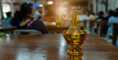 Low light view with flare. Copy space of a golden bottle is on table. For pouring water to receive blessings from the monk. It is Buddhist ritual.の写真素材