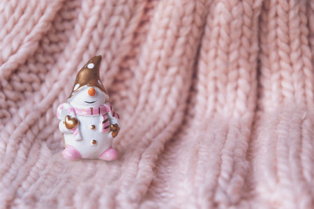 Close up picture of snowman on pink knitted pattern, as Christmas copy space wallpaper with empty space on side. Cozy picture with small figure of winter holidays in show time. New Year background.の写真素材