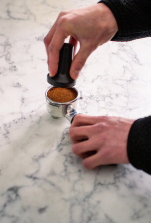 Barista tampering ground coffee in portafilter using tamper. Close-up fresh coffee preparation...