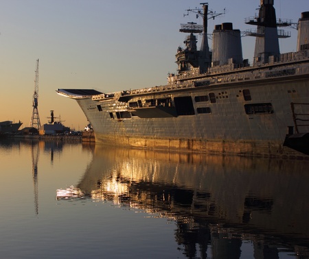 An old aircraft carrier during late evening being reflected in the water by the late sunの写真素材