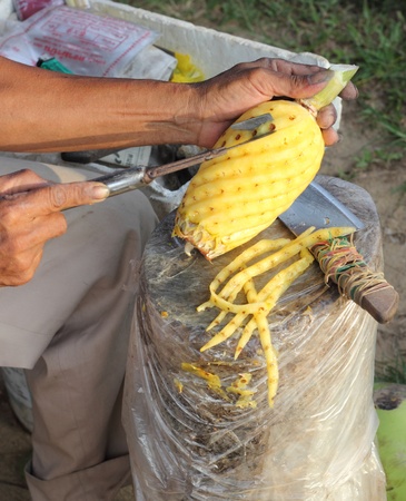Market trader carving a pineapple ready for buying customers to eatの写真素材