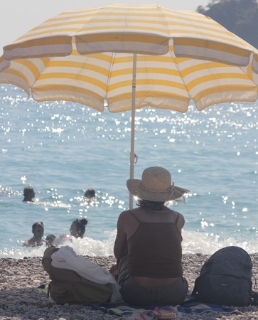 TURKEY,OLUDENIZ, 28th JULY 2013 - A woman wearing a hat sitting alone on a beach under an umbrella at Oludeniz in Turkeyのeditorial素材