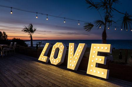wedding hall interiors and decorations illuminated love inscription against the background of the evening sky with palm trees, a sea bay in the background during the blue hourの写真素材