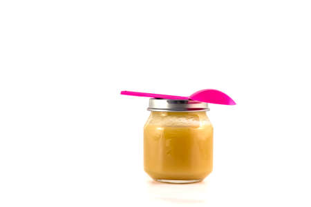 Baby fruit puree in the pot with a plastic spoon on a white backgroundの写真素材