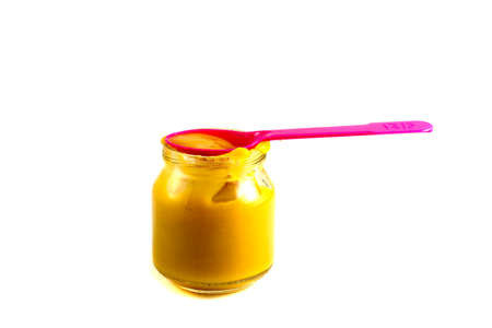 Baby fruit puree in the pot with a plastic spoon on a white backgroundの写真素材