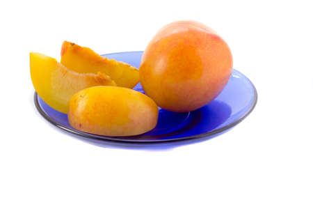 Yellow plum and three whole cloves on a blue saucer on a white backgroundの写真素材