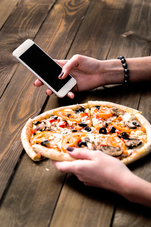 hands of a woman ordering pizza with a device over a wooden workspace table. All screen graphics are made up.の写真素材