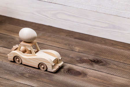 Happy easter! Wooden toy retro car carries eggs on a wooden background. Easter conceptual backgroundの写真素材