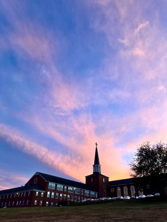 Sunset at the main historical building of a Christian seminary in South Hamilton, MA, USA. 
There is a cross at the top of the main building. 
Colorful sky as background.の写真素材
