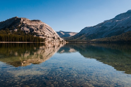 View of lake in afternoon light  Calm water reflects hill on oposite side of lake  Water is very clear a can be seen stones and rocks on bottom of lake の写真素材