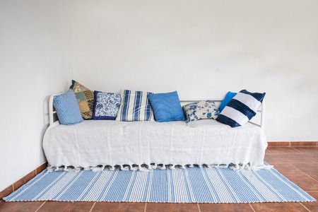 Horizontal view of white couch with many pillows and blue/white carpet in front. Clean white wall. Interior design concept.の写真素材