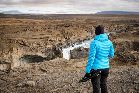 Female hiker looking at Aldeyjarfoss waterfall, Iceland. Female photographer holding a tripod.の写真素材