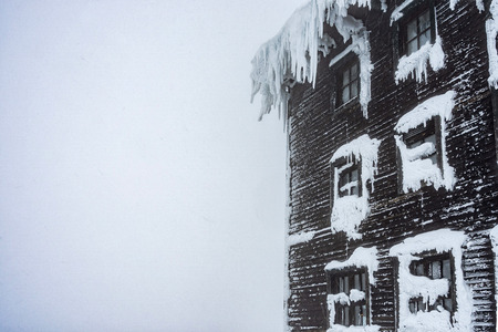 Detail view of mountain cabin in a misty weather. Foggy weather in a snow covered landscape.