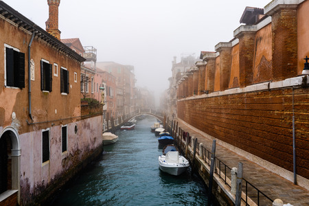 Foggy (misty) day in Venice. Canal, historical old houses and boats with gondolas in thick fog, Venice. Italy.の写真素材