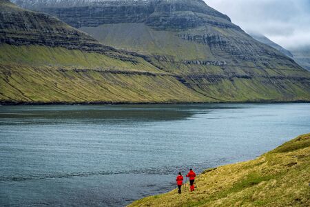 Two female hikers walking on a trail next to a wide fjord in Faroe Islands.