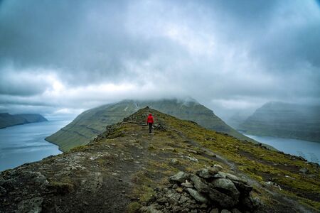 Young female hikers walking on a trail next to a wide fjord in Faroe Islands.の写真素材