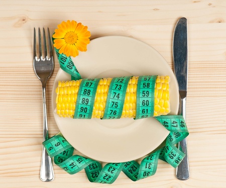 Sweetcorn with tape measure and cutlery over wooden surfaceの写真素材
