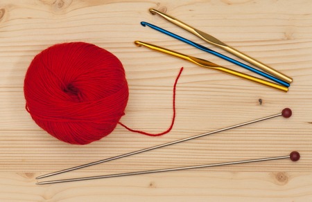 Knitting  hook and spokes with woolen threads over wooden surface