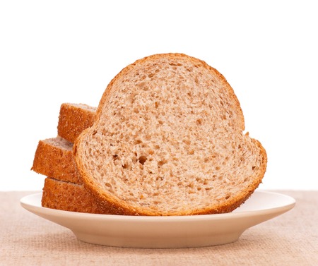 Slices of fresh bread with bran on a saucer on a burlap over white background