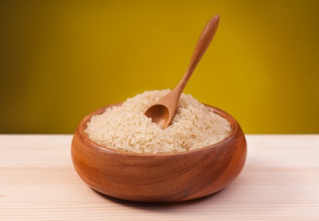 White rice in a bamboo bowl on a wooden surface over dark yellow backgroundの写真素材