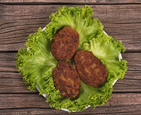 Tasty baked cutlets with green lettuce leaves over wooden surfaceの写真素材