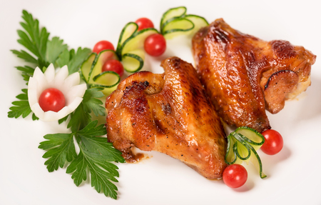 Baked chicken wings with fresh vegetables over white plate backgroundの写真素材
