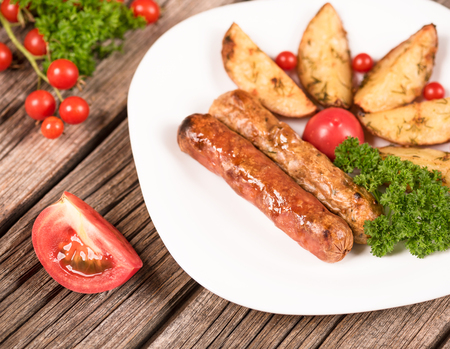 Delicious grilled wieners with fried potatoes and vegetables over wooden backgroundの写真素材