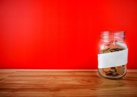 Coins in a glass jar on a wooden floor. Pocket savings from coins in the bank. Piggy bank in glass jar with coinsの写真素材