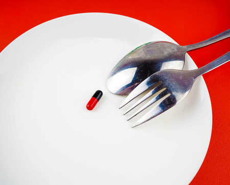 Medical pills on white plate with fork and spoon