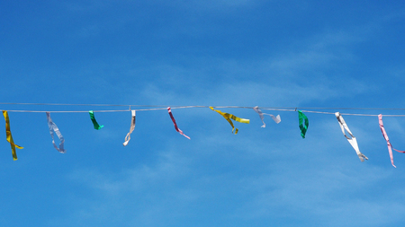 Several colorful streamers on a horizontal string with a blue sky background.の写真素材