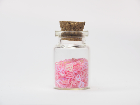 Isolated profile of tiny pink plastic hearts are in a small glass bottle with a cork stopper.の写真素材