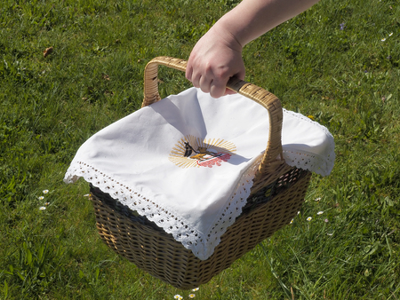 Woven basket with traditional european Easter cloth being carried over grass.の写真素材
