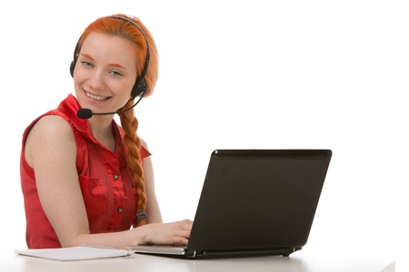 Attractive young female call centre operator, receptionist or personal assistant sitting at a laptop wearing a headset and smiling at the cameraの写真素材