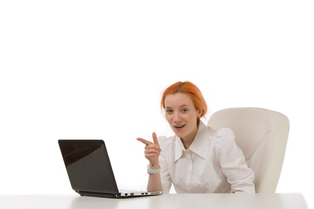 Smiling attractive young redhead businesswoman sitting at a desk pointing at the screen on her laptop which is facing away from the cameraの写真素材