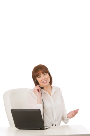 Pretty young female receptionist or call centre operator sitting at a desk in front of a laptop computer chatting on her headset microphoneの写真素材