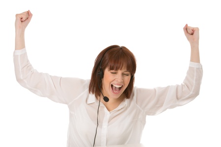 Jubilant woman wearing a headset cheering and raising her fists in the air as she celebrates good news isolated on whiteの写真素材