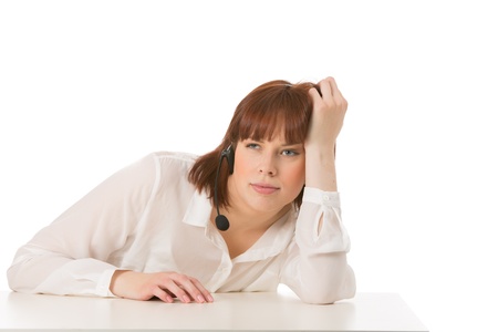 Bored woman wearing a headset leaning on a table with a distant expression while waiting for a call to come in, upper body on whiteの写真素材