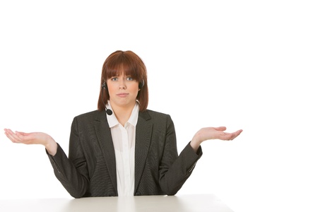 Attractive young businesswoman seated at her desk shrugging her shoulders and raising her hands in the air to show her ignorance or indifferenceの写真素材