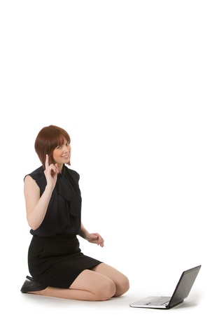 Attractive young woman kneeling on the floor alongside her laptop computer chatting on her mobile phone, on whiteの写真素材