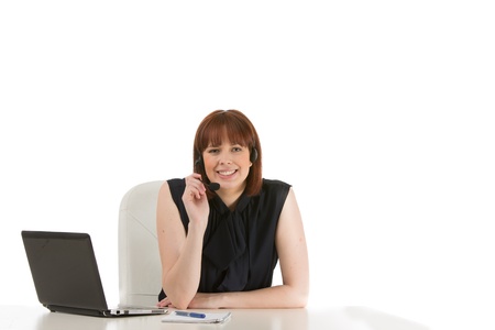 Smiling receptionist, secretary or call centre operator seated at her desk with a laptop computer wearing a headsetの写真素材
