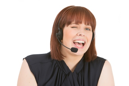 Laughing call centre operator winking as she listens to a conversation on her headset, head and shoulders portrait on whiteの写真素材