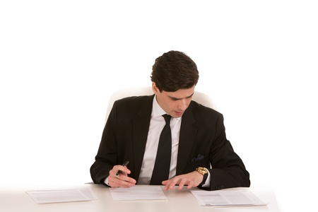 Hardworking young businessman sitting working at his desk making notes from an article that he is reading, on a white backgroundの写真素材