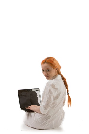 Woman working on a laptop sitting on the floor with it balanced on her knees looking back over her shoulder at the viewer, on whiteの写真素材
