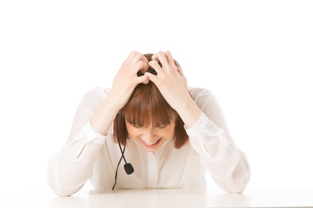 Frustrated businesswoman wearing a headset holding her head in her hands and gnashing her teeth as she sits at a deskの写真素材