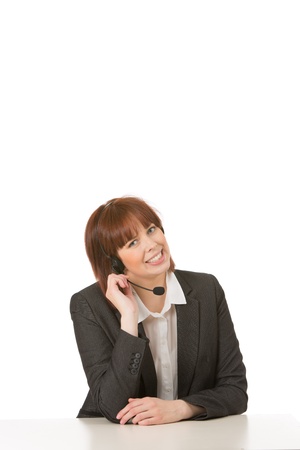 Friendly smiling female call centre operator listening to a conversation on her headset while seated at a table, on whiteの写真素材