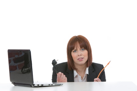Ignorant woman peering over the top of a table with a laptop on it holding computer cables in her hands with a look of confusion, on whiteの写真素材