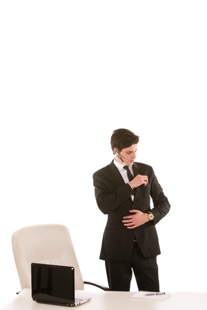 Businessman putting something in the pocket of his suit jacket while standing behind his desk and laptop computer, on whiteの写真素材