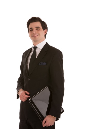 Handsome young smiling successful business man standing with a black folder under his arm looking down at the camera isolated on whiteの写真素材