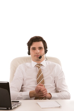 Handsome businessman wearing a headset seated at his desk with a laptop looking at the camera on a white backgroundの写真素材