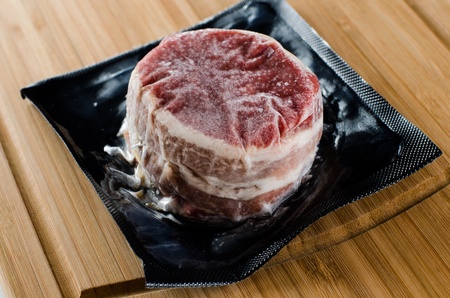 Picture of a Frozen Vacuum Sealed Bacon Wrapped Fillet Mignon sitting on a butcher block ready for cooking の写真素材